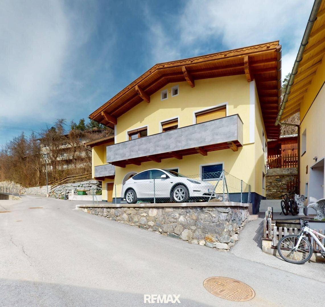 Ansicht des gelben Hauses von der Seite mit geparktem Auto auf einer erhöhten Fläche.