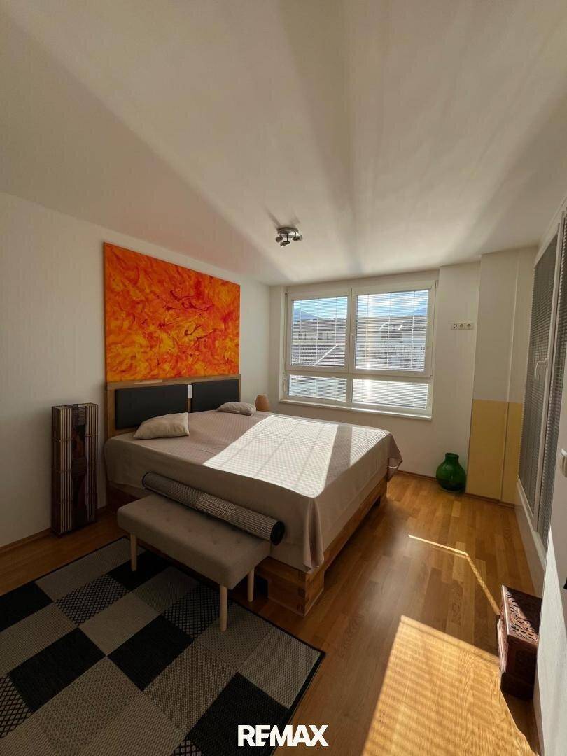 Helles Schlafzimmer mit Holzboden und großem Fenster, das eine angenehme Atmosphäre schafft.
