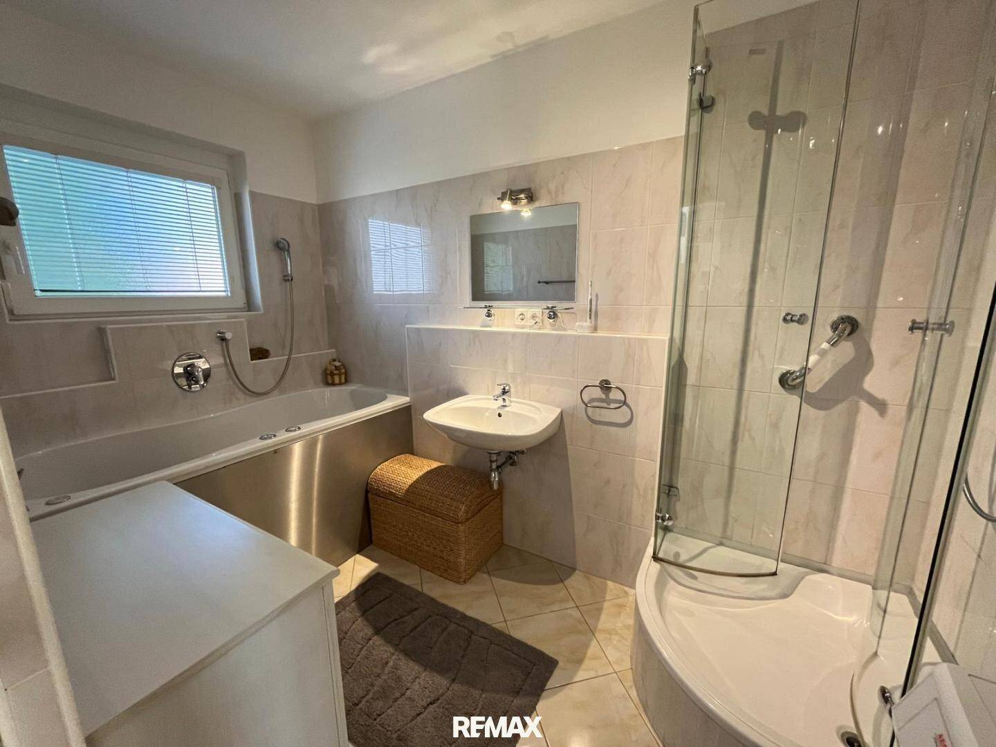 Modernes Badezimmer mit Badewanne, Dusche und Fenster, ausgestattet mit hellen Fliesen.