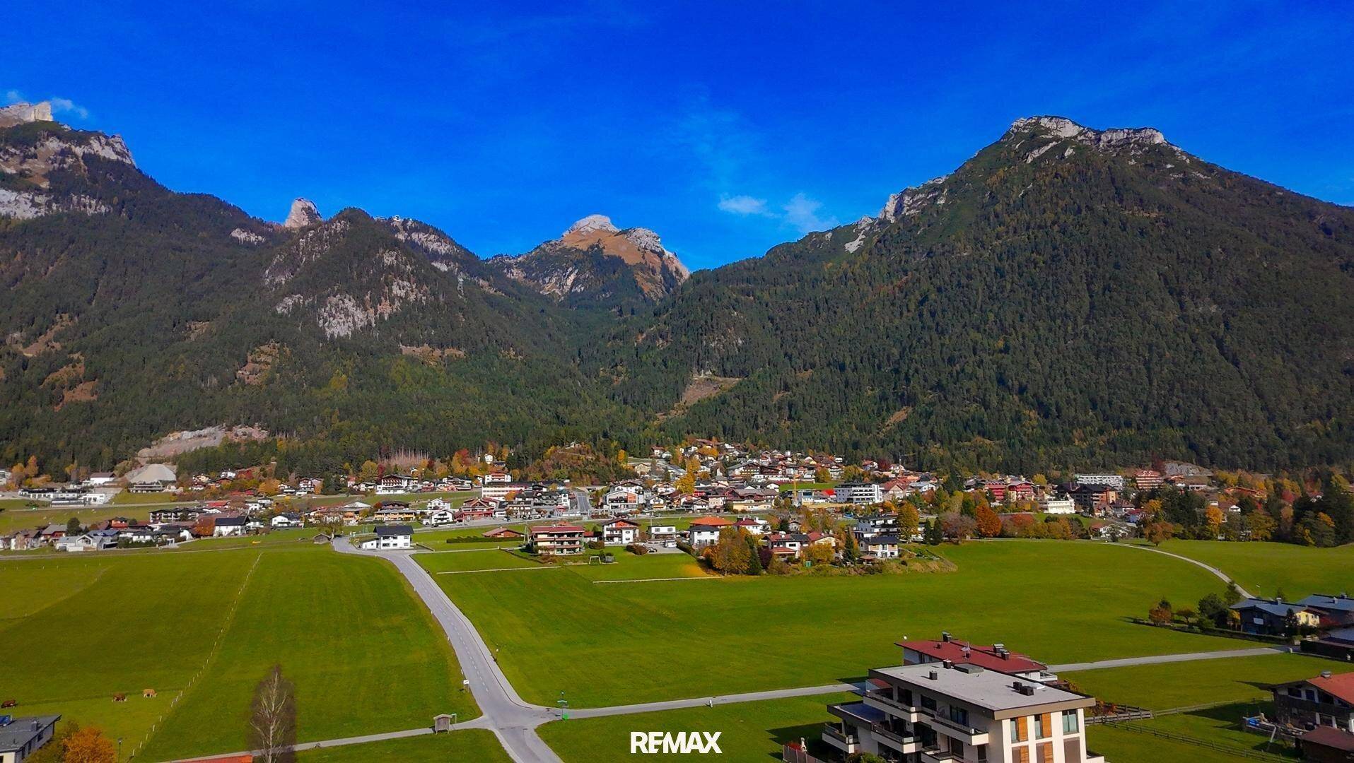 Panoramablick auf ein idyllisches Dorf, eingebettet in eine grüne Landschaft mit imposanten Bergen.