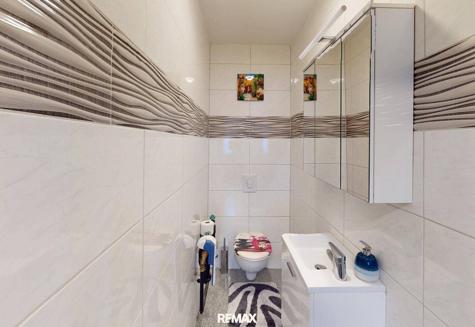 Kleines Gäste-WC mit weißen Fliesen, wandhängendem WC und modernem Waschbecken.