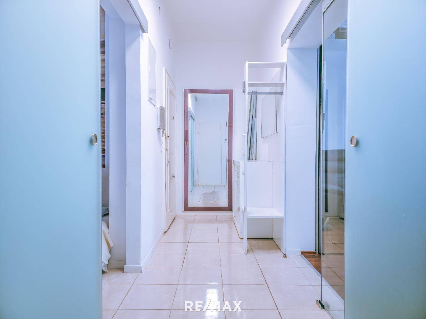 Langer Flur mit Fliesenboden und Spiegel, der zu weiteren Räumen führt.