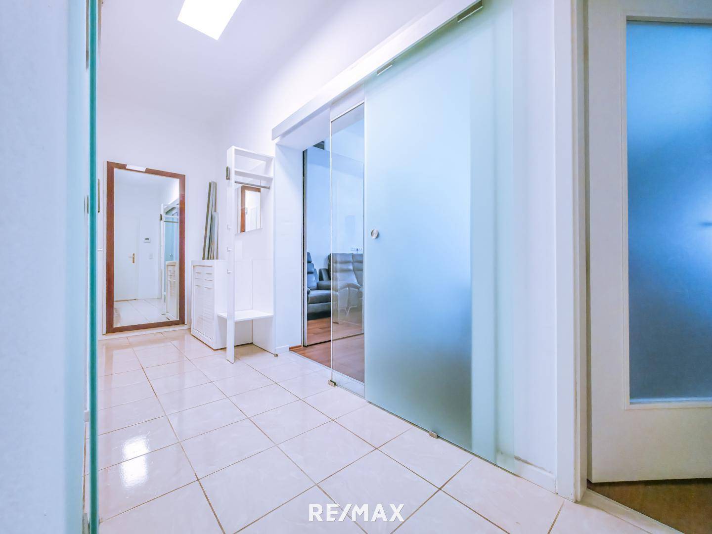 Heller Flur mit Fliesenboden und Glasschiebetüren.