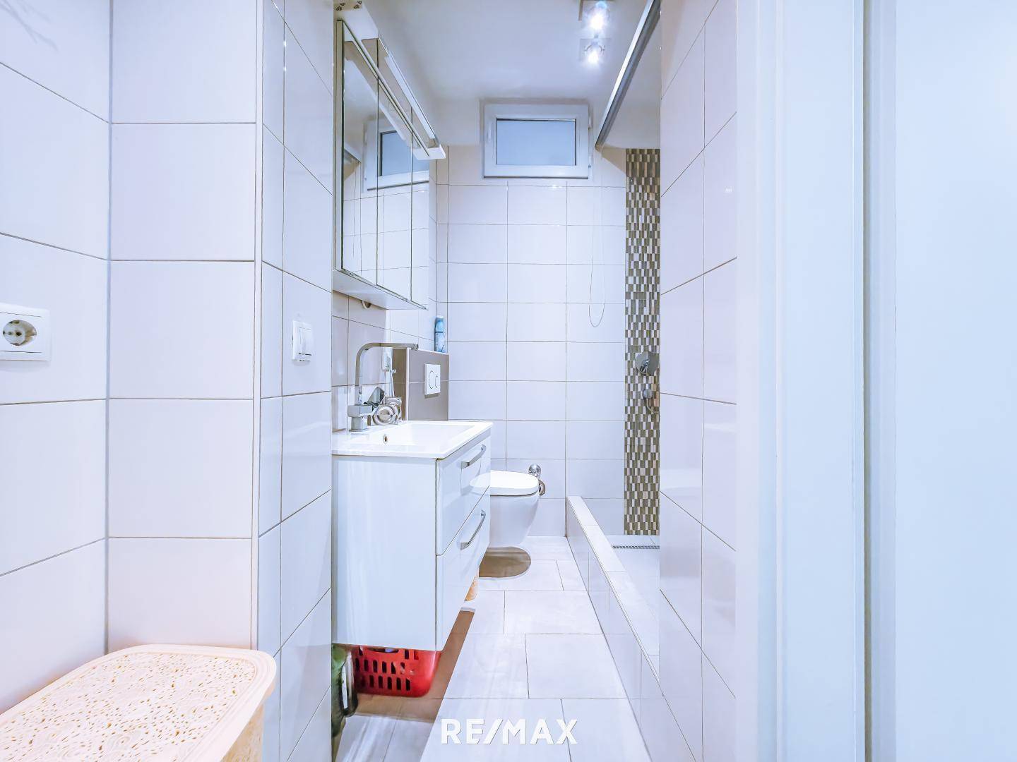 Helles Badezimmer mit weißen Fliesen, Waschbecken und Badewanne.