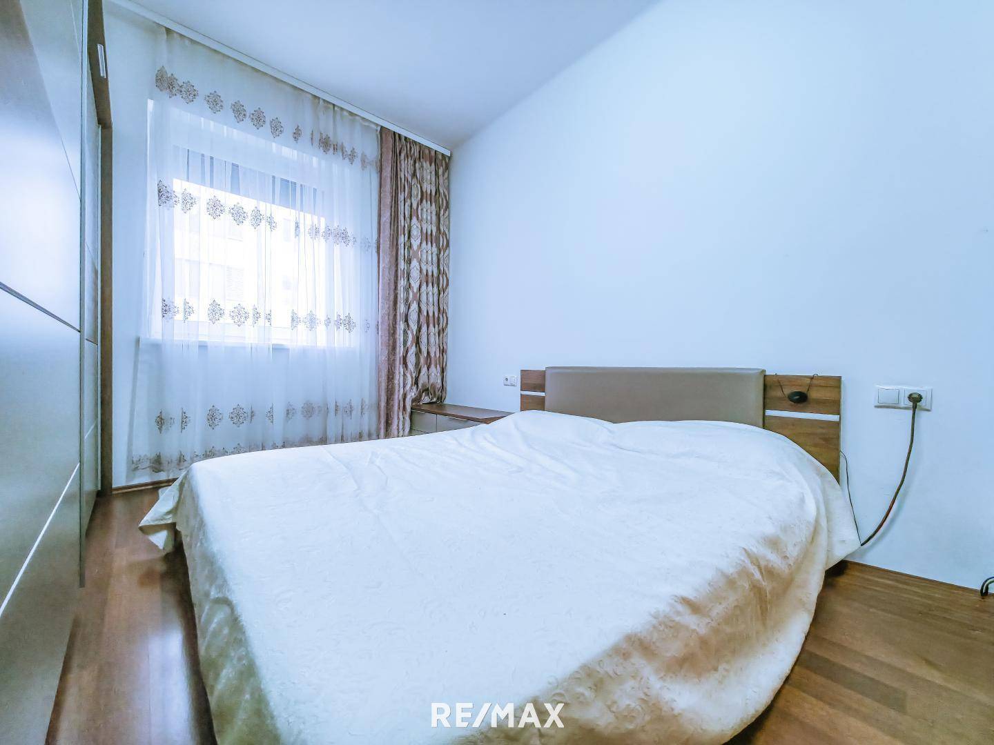 Schlafzimmer mit Holzboden, Doppelbett und großem Fenster.