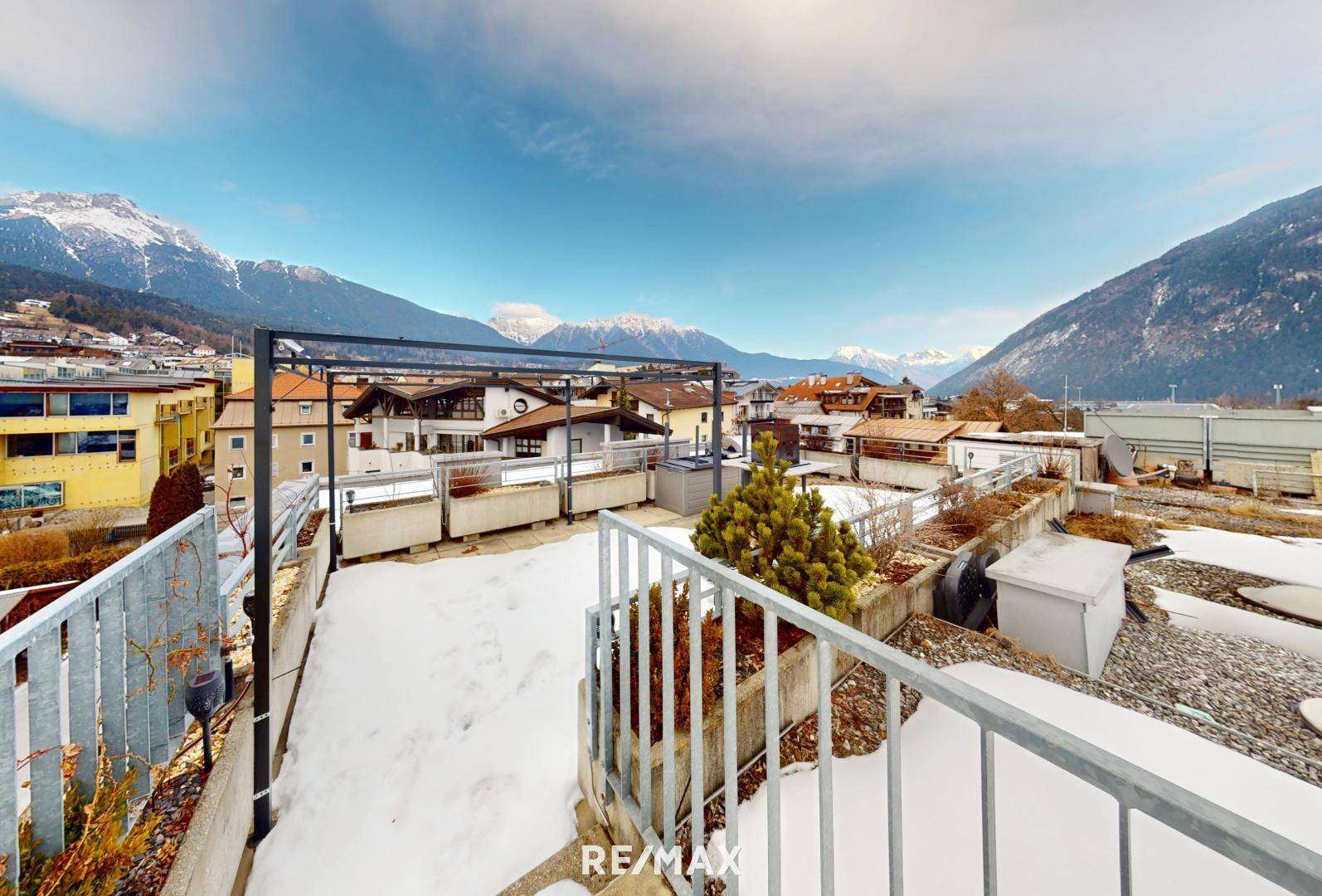 Dachterrasse mit Bergblick, teilweise schneebedeckt und mit Metallgeländer.