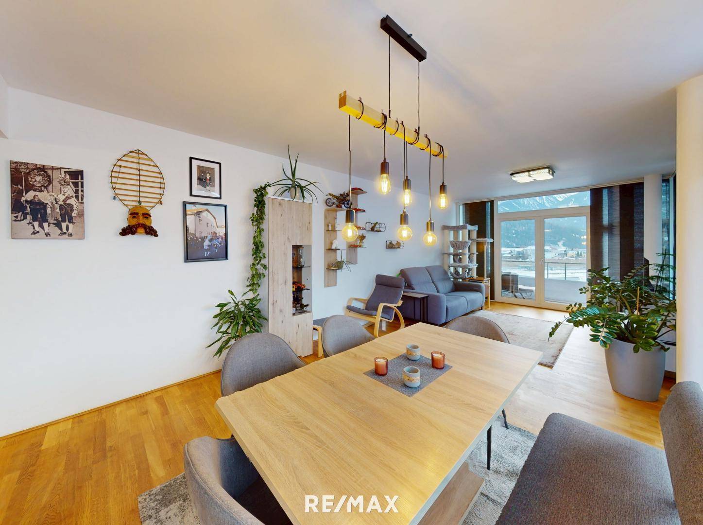 Geräumiger Wohn-Essbereich mit Holztisch, modernen Leuchten und Blick auf die Berge.