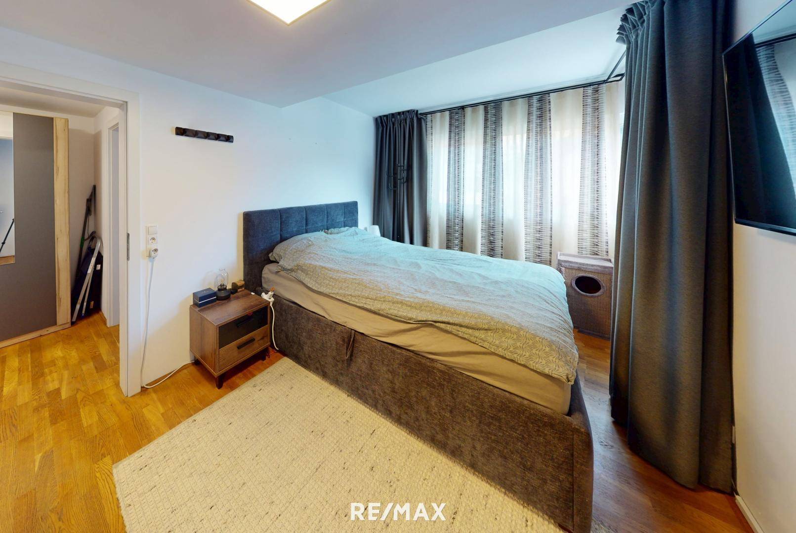 Schlafzimmer mit großem Bett, Holzboden und dunklen Vorhängen für Privatsphäre.