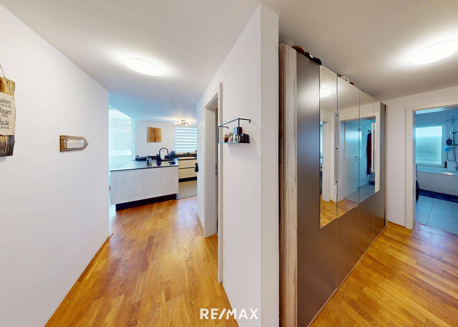 Heller Flur mit Holzboden, Spiegelschränken und Blick in die Küche.