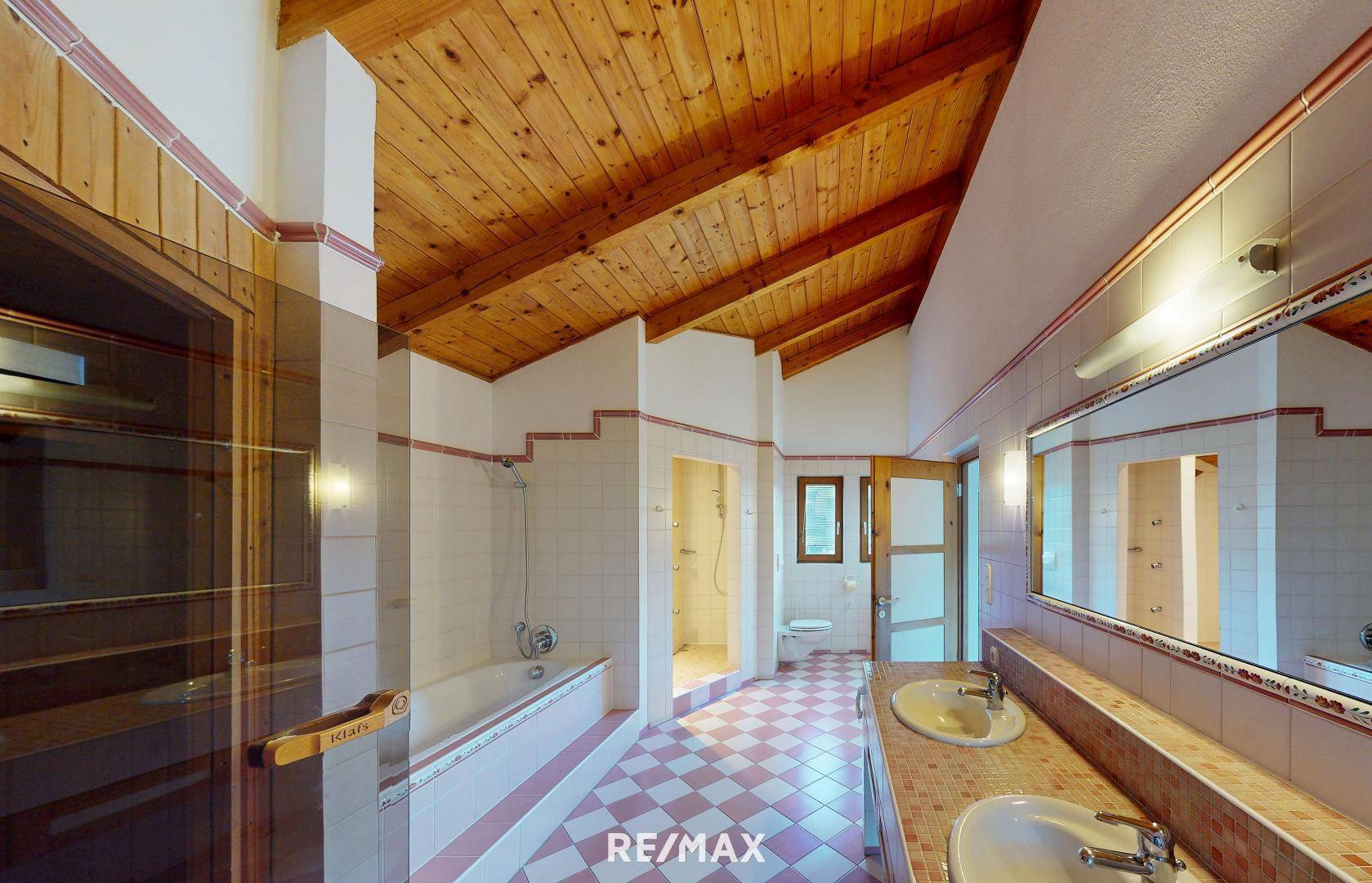 Großes Badezimmer mit Doppelwaschbecken, Badewanne, Sauna und Holzbalkendecke.