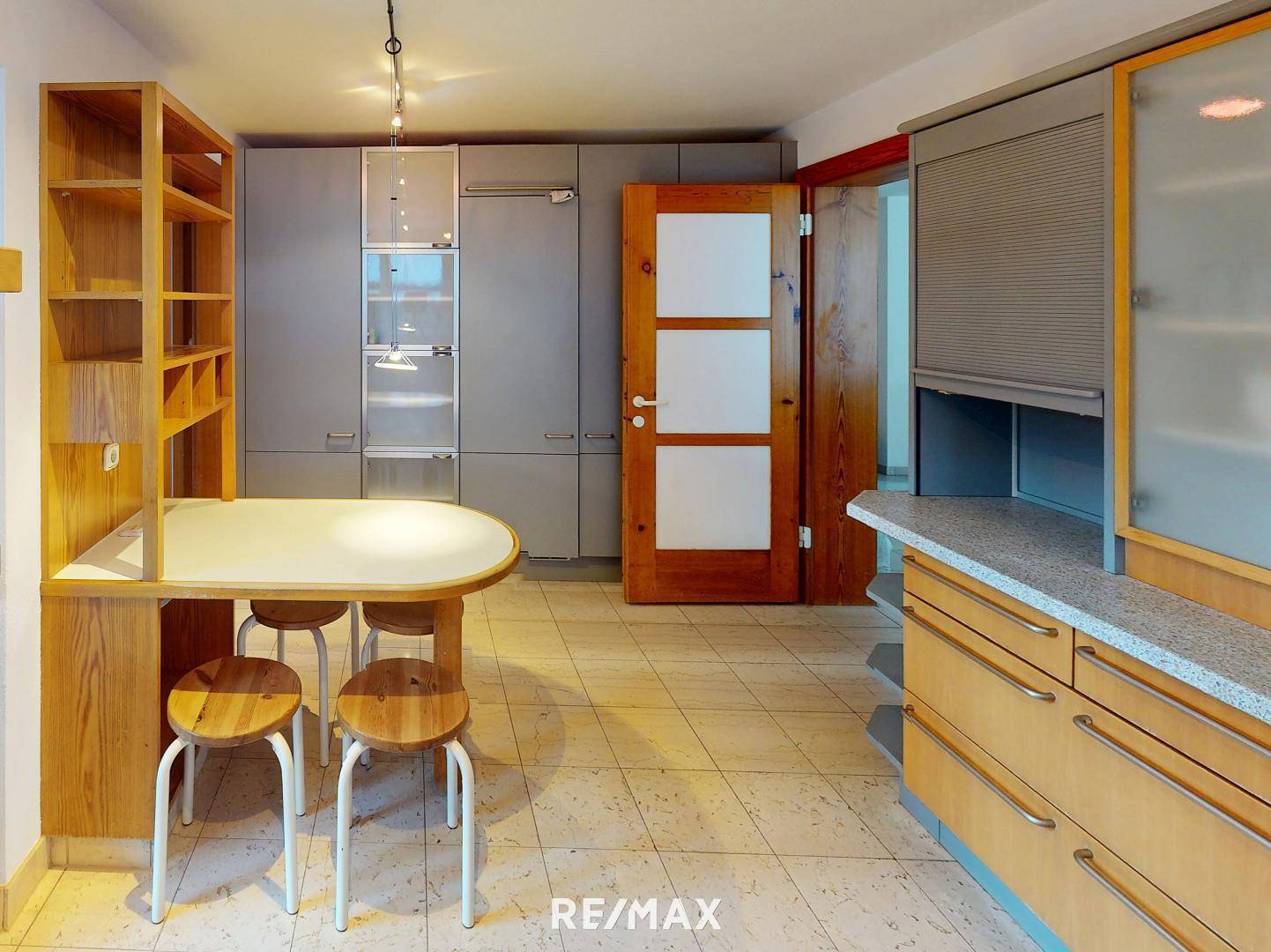 Küche mit Essbereich, Fliesenboden und modernen Schränken in Grau und Holz.