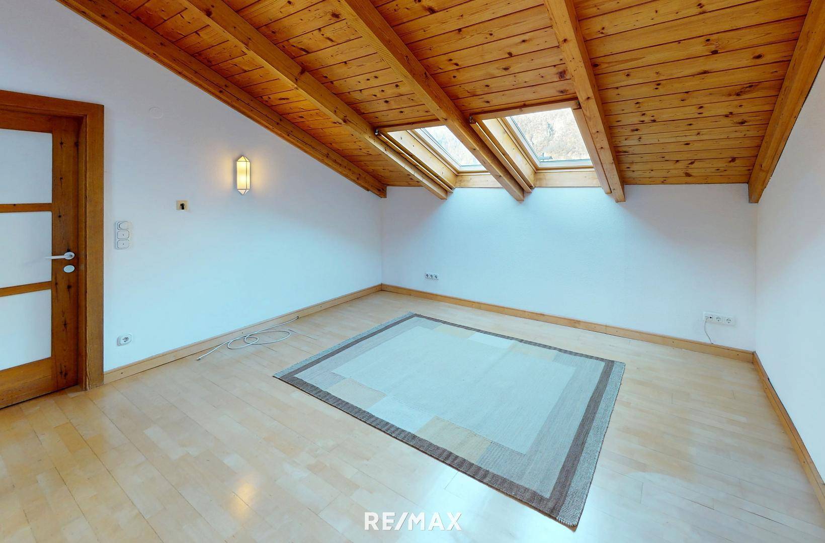 Helles Dachzimmer mit Holzbalkendecke, Parkettboden und Dachfenstern für natürliches Licht.