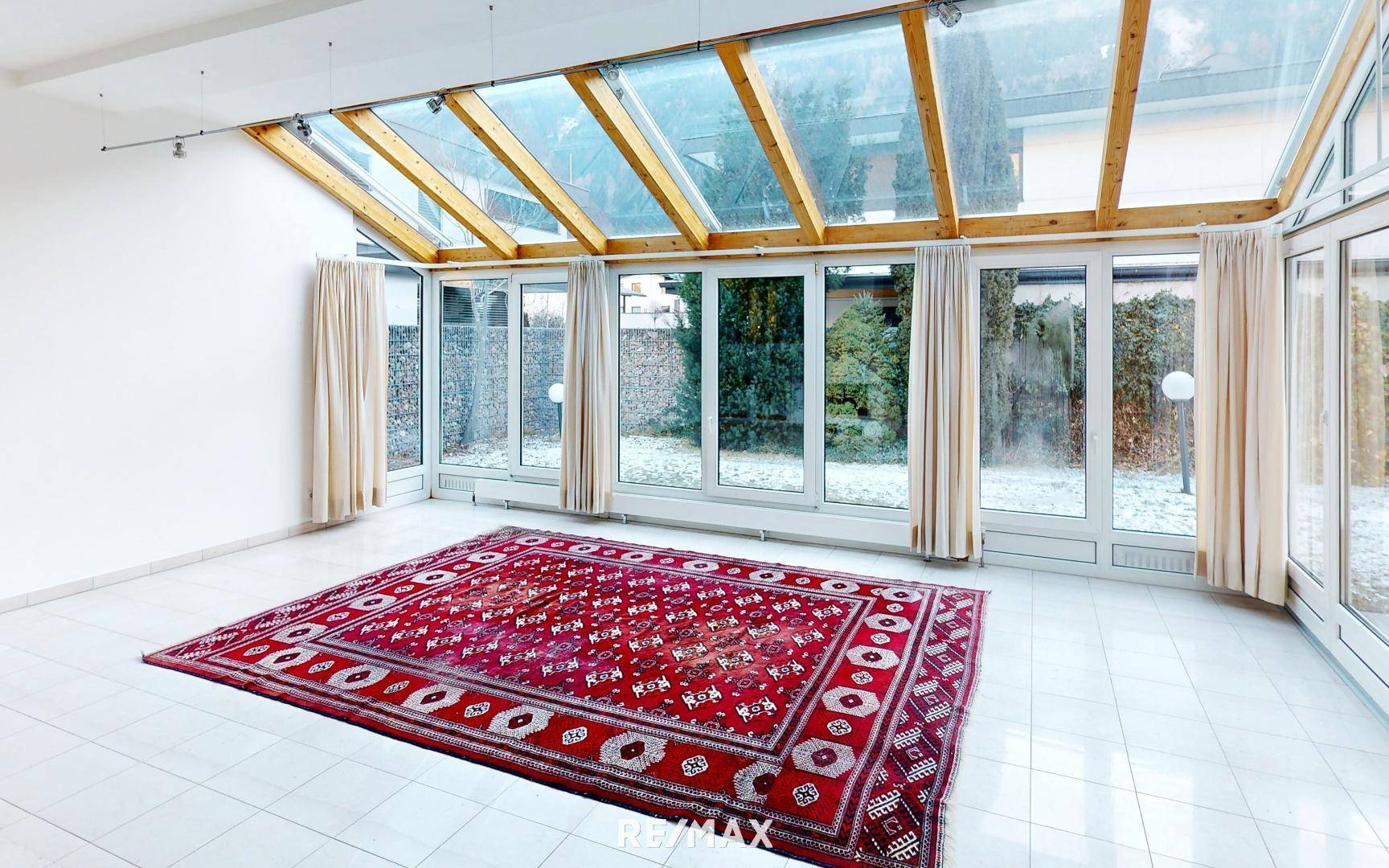 Heller Wintergarten-Wohnbereich mit Fliesenboden und großflächigen Glasfronten.