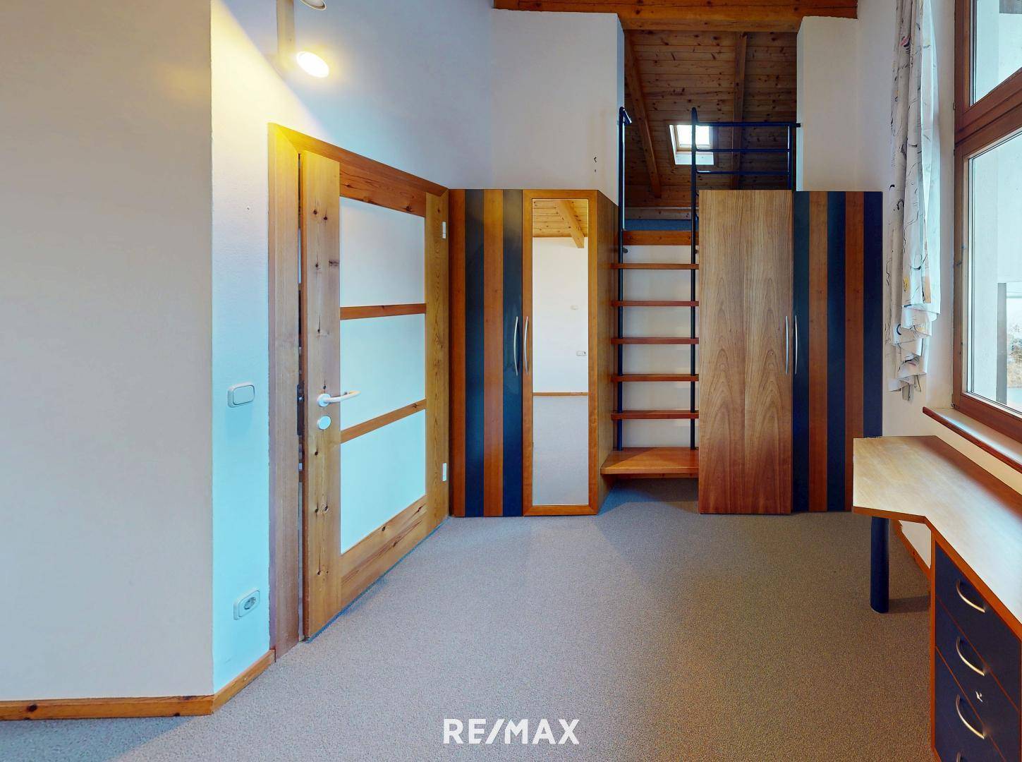 Dachzimmer mit Holzbalkendecke, Teppichboden und praktischen Einbauschränken.