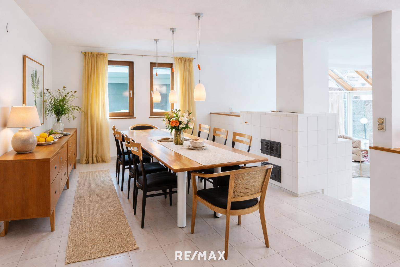 Geräumiger Essbereich mit großem Holztisch, Fliesenboden und traditionellem Kachelofen.