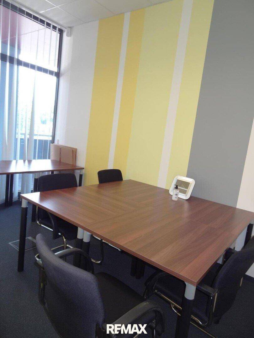 Heller Konferenzraum mit großen Fenstern, Holztischen und einer modern gestreiften Wand in Gelb und Grau.