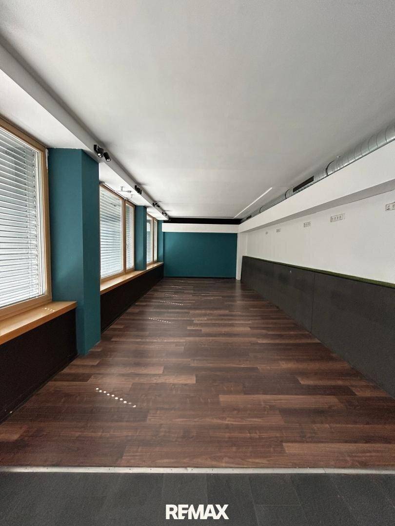 Langer, heller Gewerberaum mit dunklem Laminatboden und modernen Wandfarben, bereit zur individuellen Gestaltung.