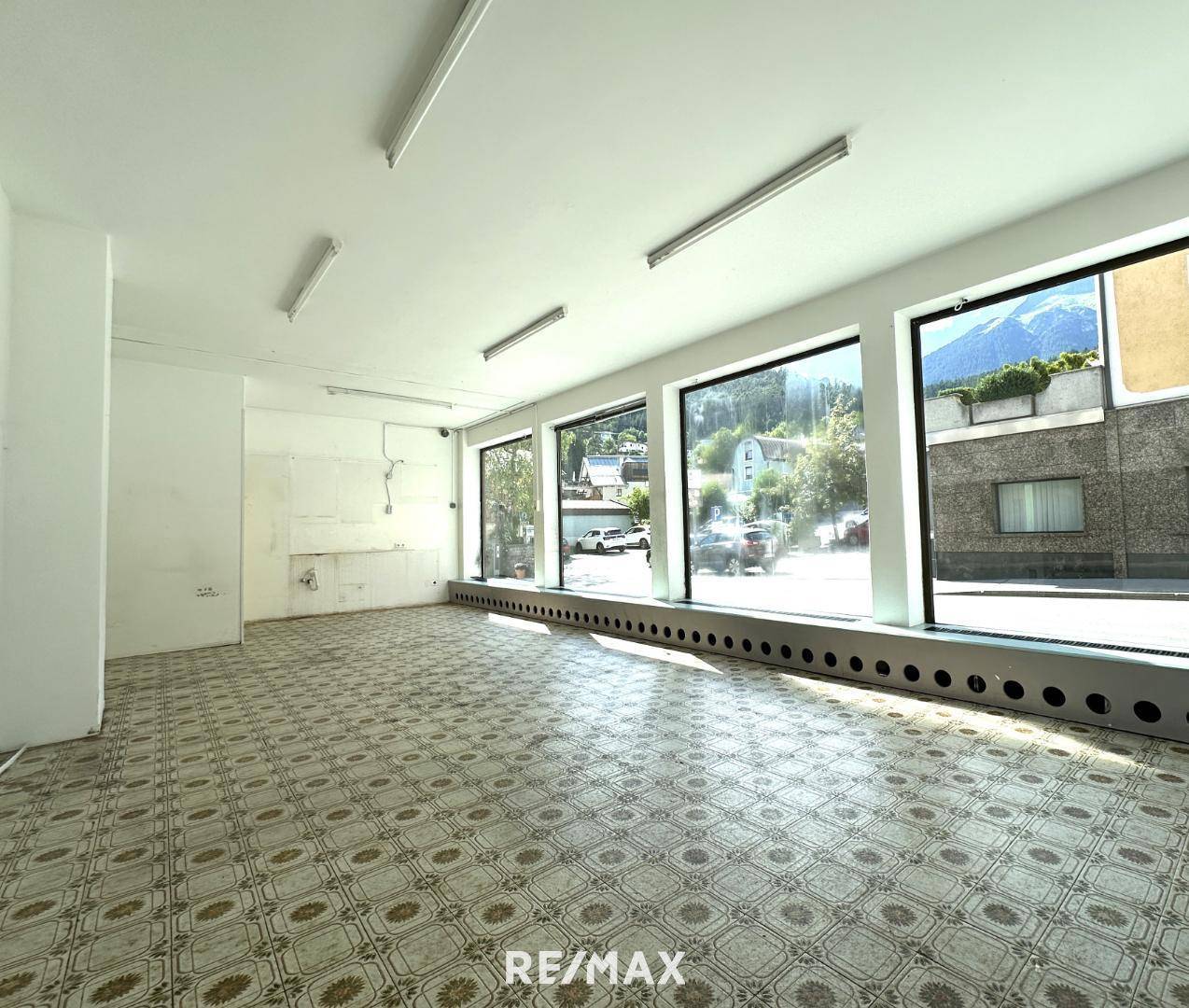Leerer Ladenraum mit großen Schaufenstern, gemustertem Boden und Blick auf die Berge, bereit zur Nutzung.