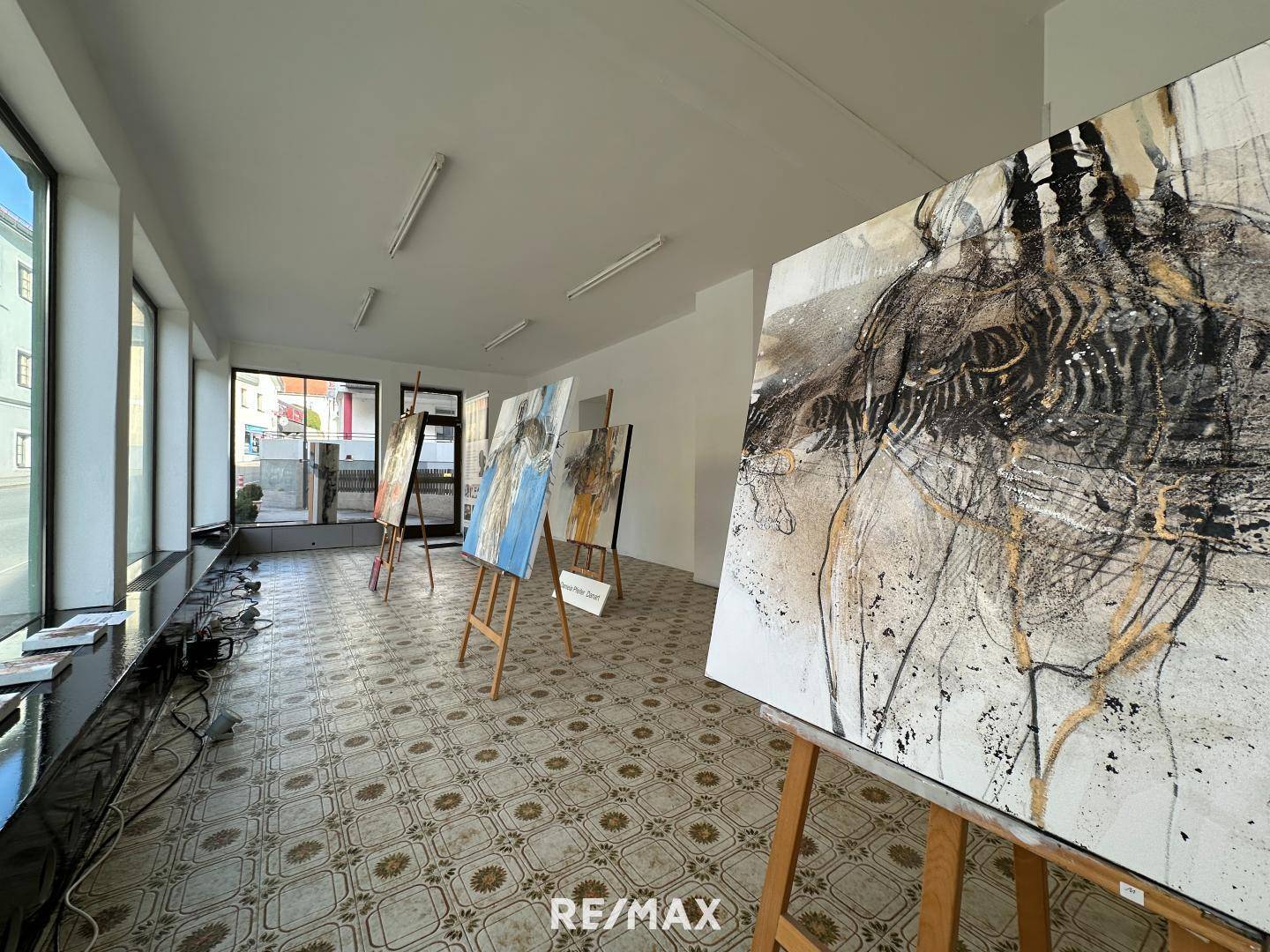 Geräumiger Ausstellungsraum mit Kunstwerken, großen Fenstern und Blick auf die Straße, gut beleuchtet.