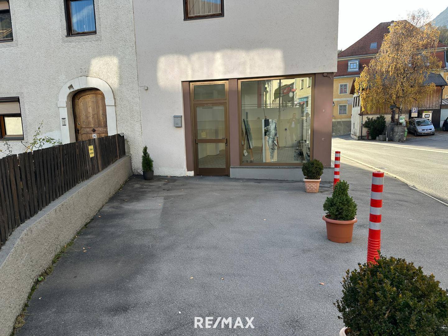 Eingangsbereich eines Gebäudes mit kleiner Zufahrt und Topfpflanzen am Straßenrand, gut zugänglich.