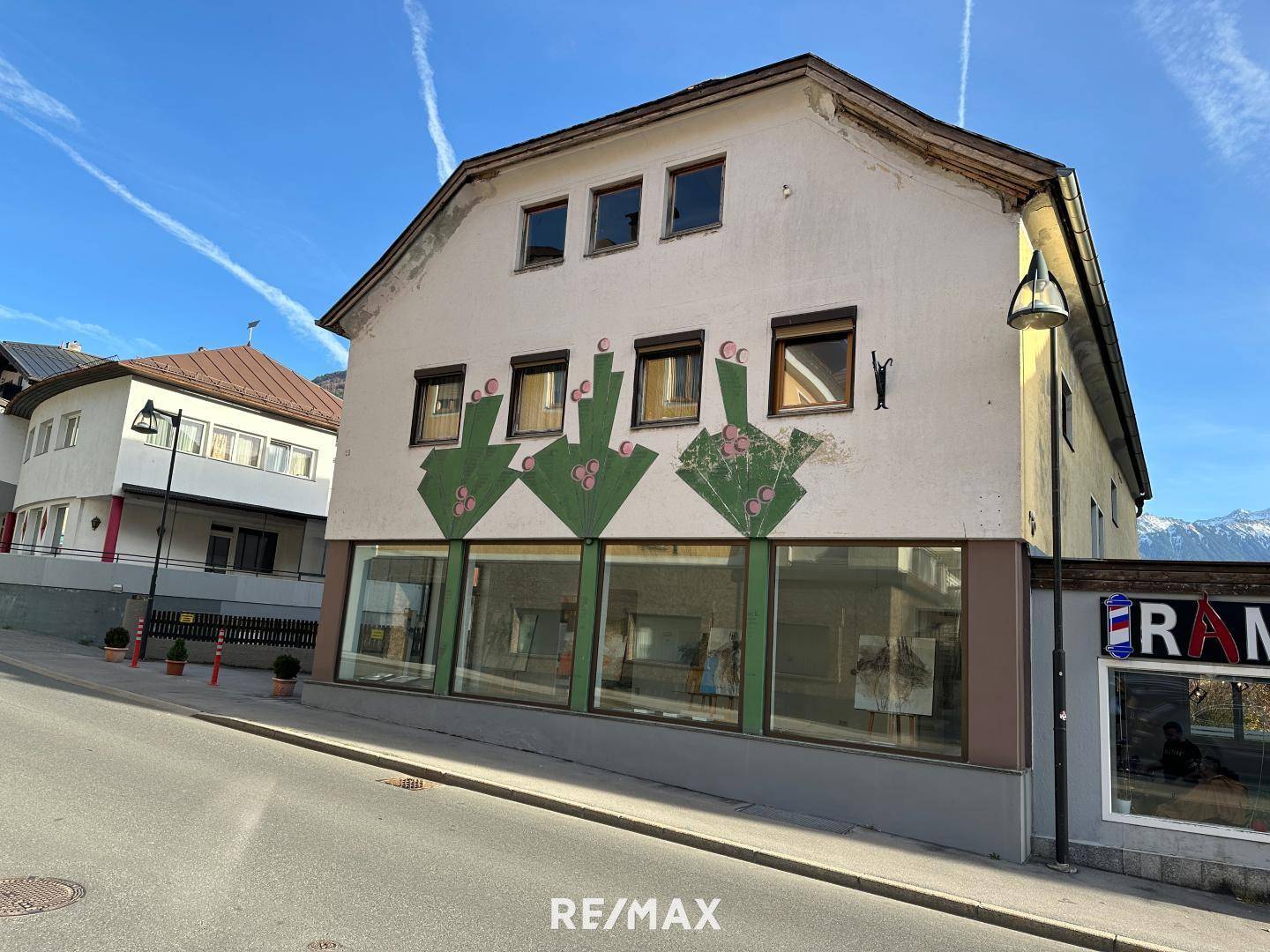 Gebäude mit Ladenfront im Erdgeschoss und Wohnungen darüber, unter blauem Himmel mit Bergblick.
