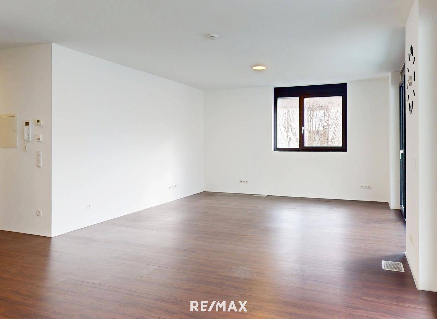 Geräumiges, helles Zimmer mit dunklem Holzboden und großen Fenstern.