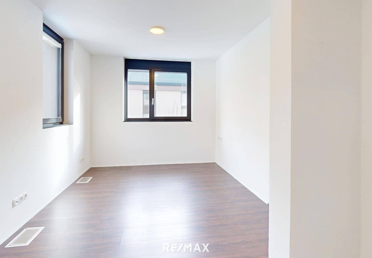 Leeres Schlafzimmer mit dunklem Holzboden und Fenster.