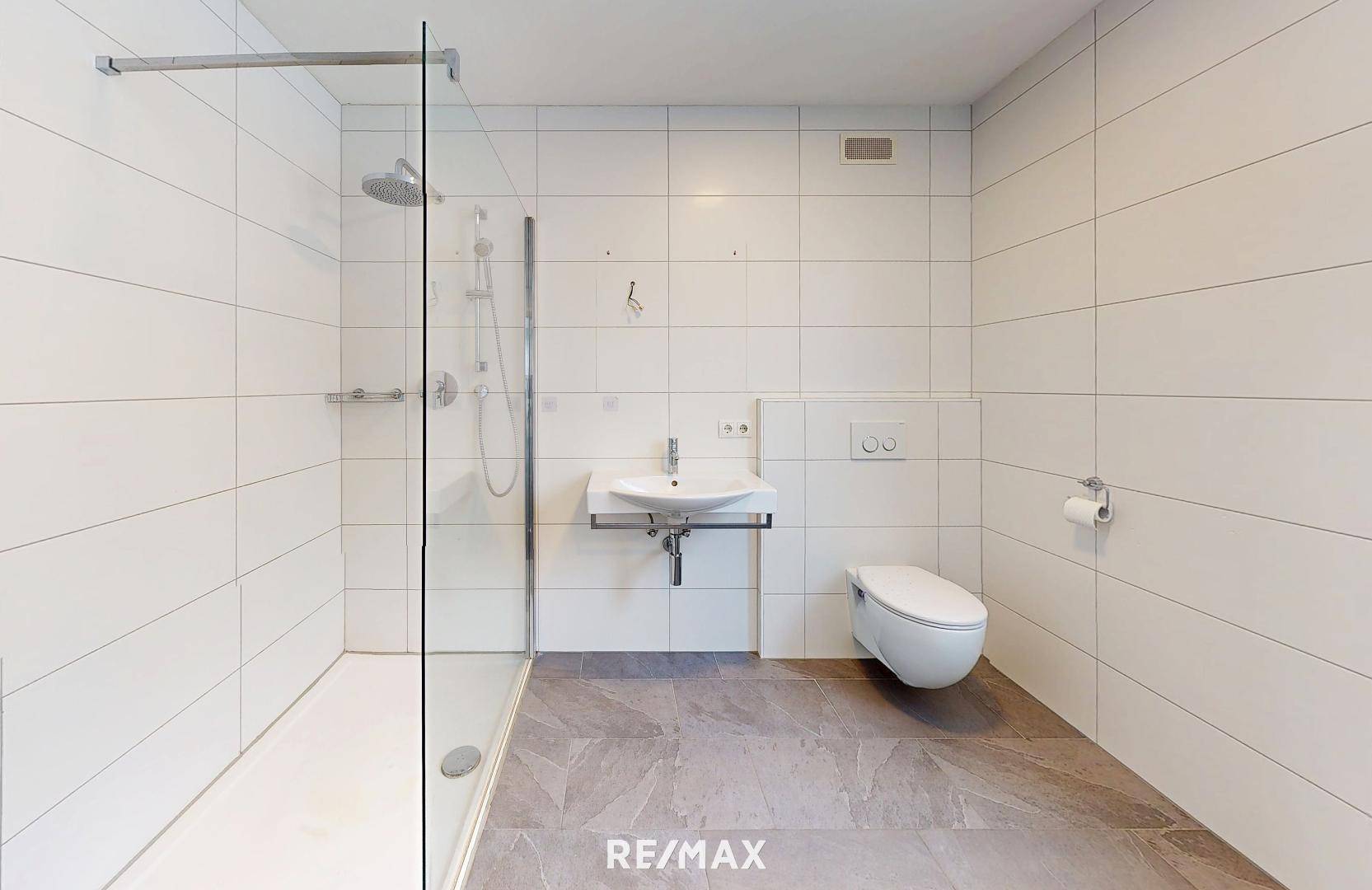 Modernes Badezimmer mit großer ebenerdiger Dusche, WC und Waschbecken.