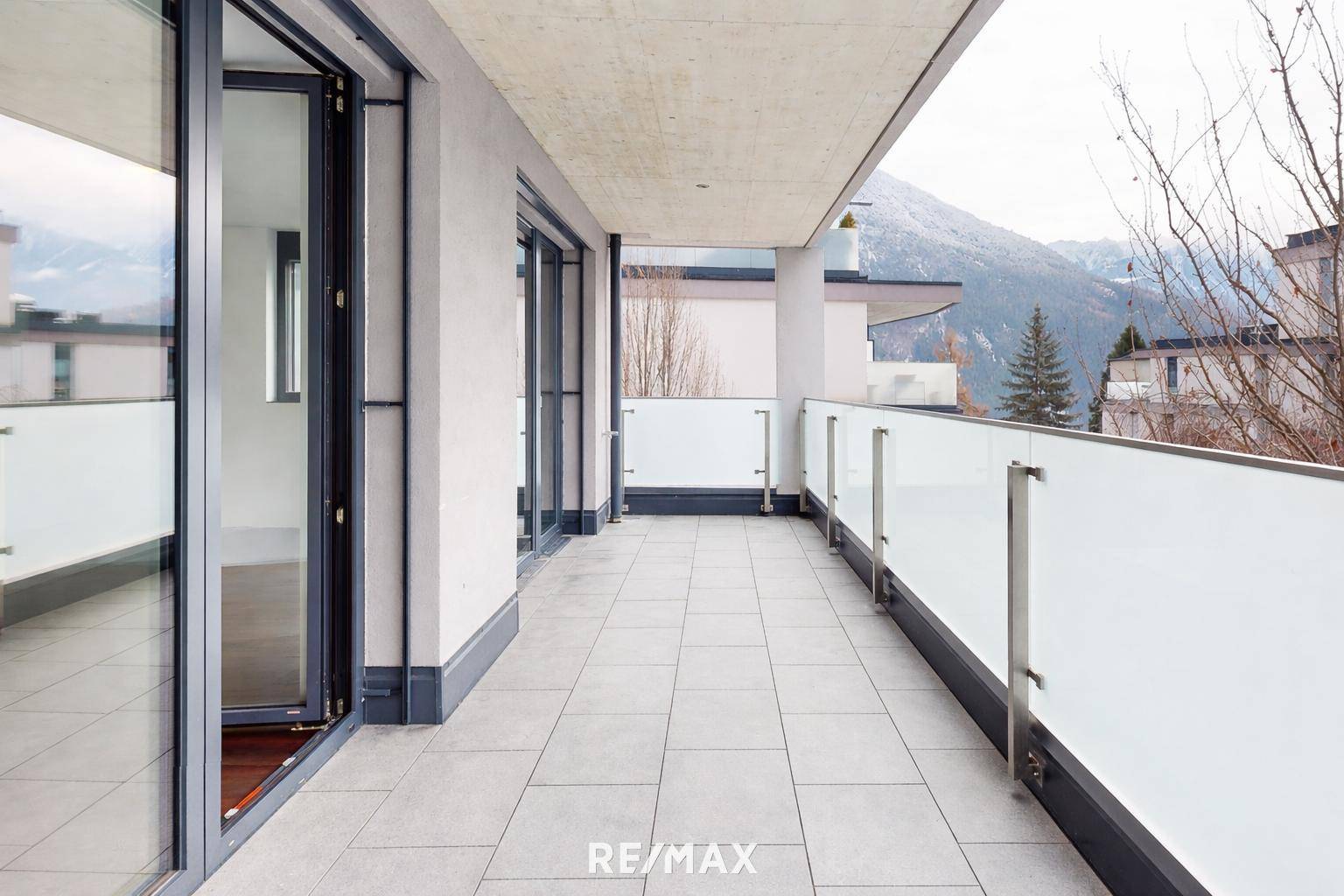 Langer Balkon mit Fliesenboden, Glasgeländer und Bergblick.