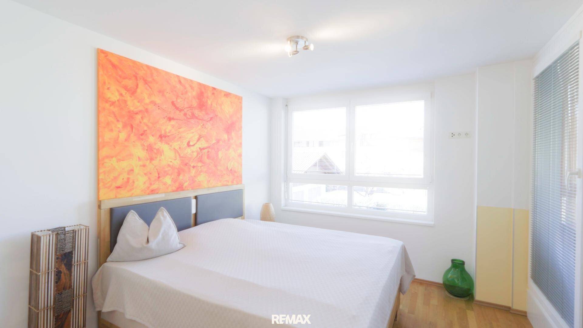 Helles Schlafzimmer mit großem Fenster, Parkettboden und modernem Bett.