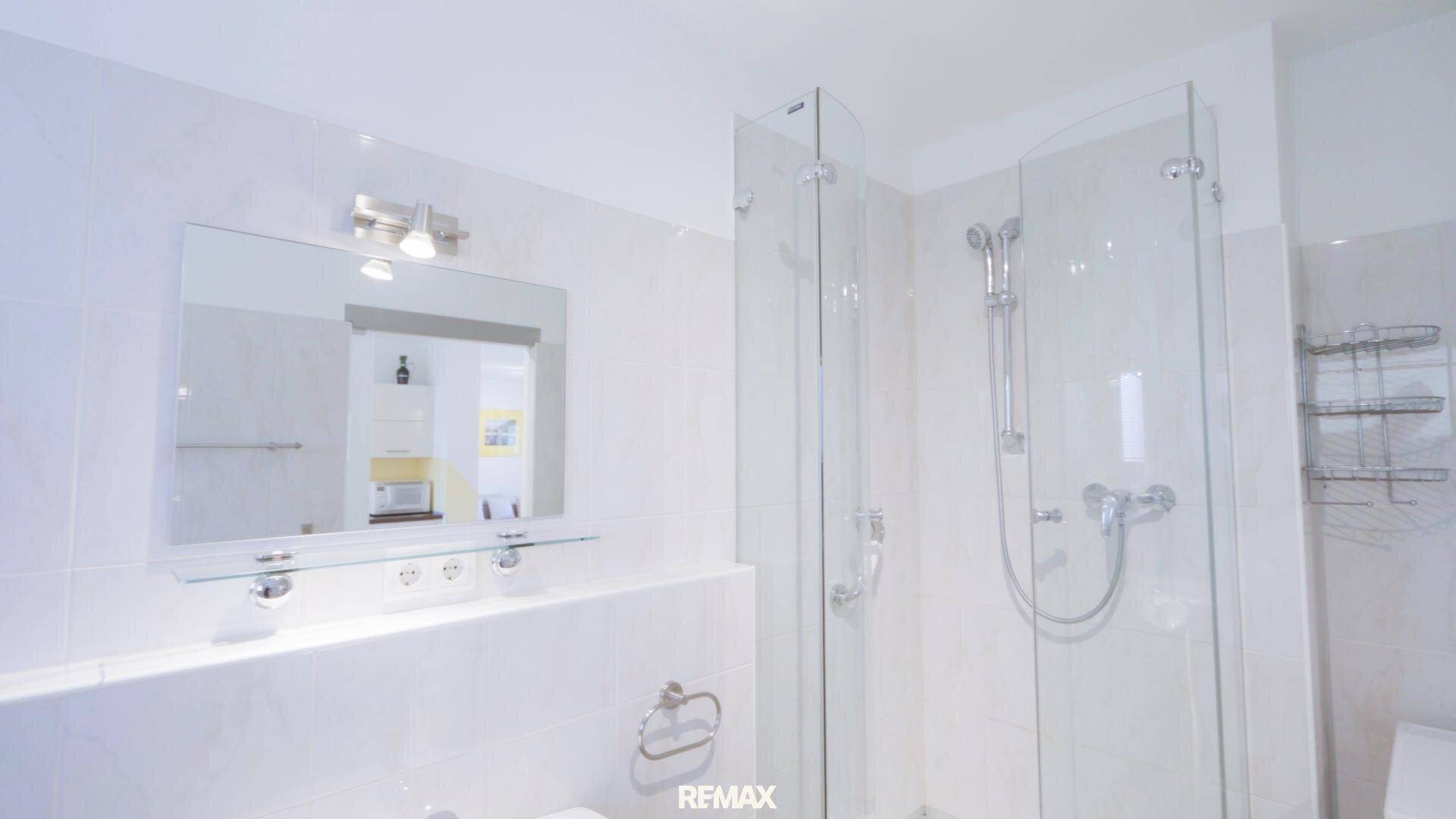 Modernes Badezimmer mit Duschkabine, Waschbecken und großem Spiegel.