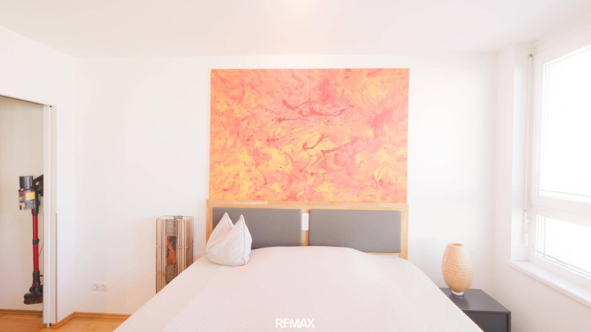 Schlafzimmer mit großem Bett, Holzboden und farbenfrohem Kunstwerk an der Wand.