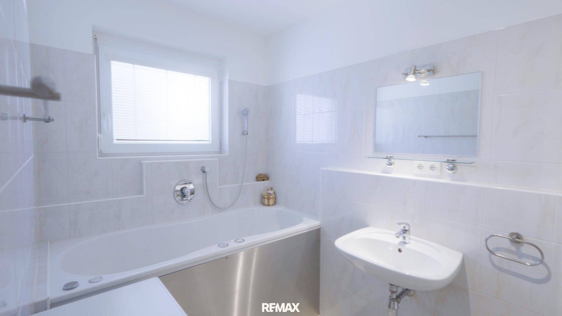 Badezimmer mit Badewanne, Waschbecken, Spiegel und hellen Fliesen.