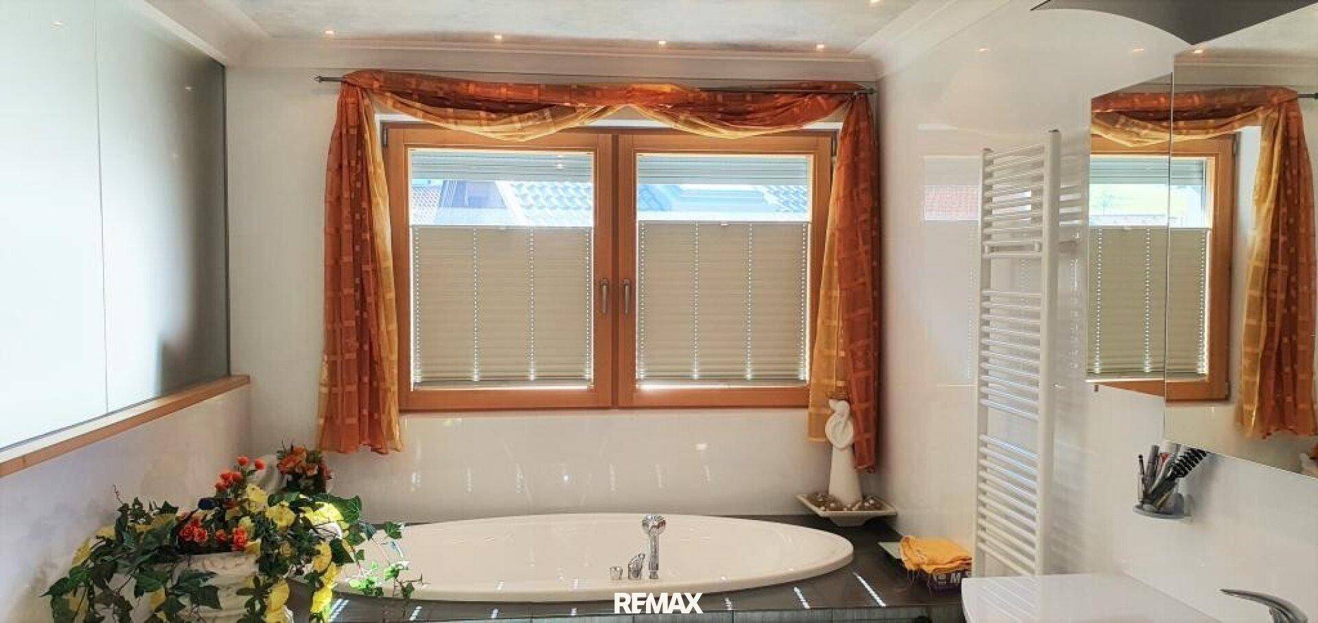 Helles Badezimmer mit Badewanne, Fenster und beheiztem Handtuchhalter.