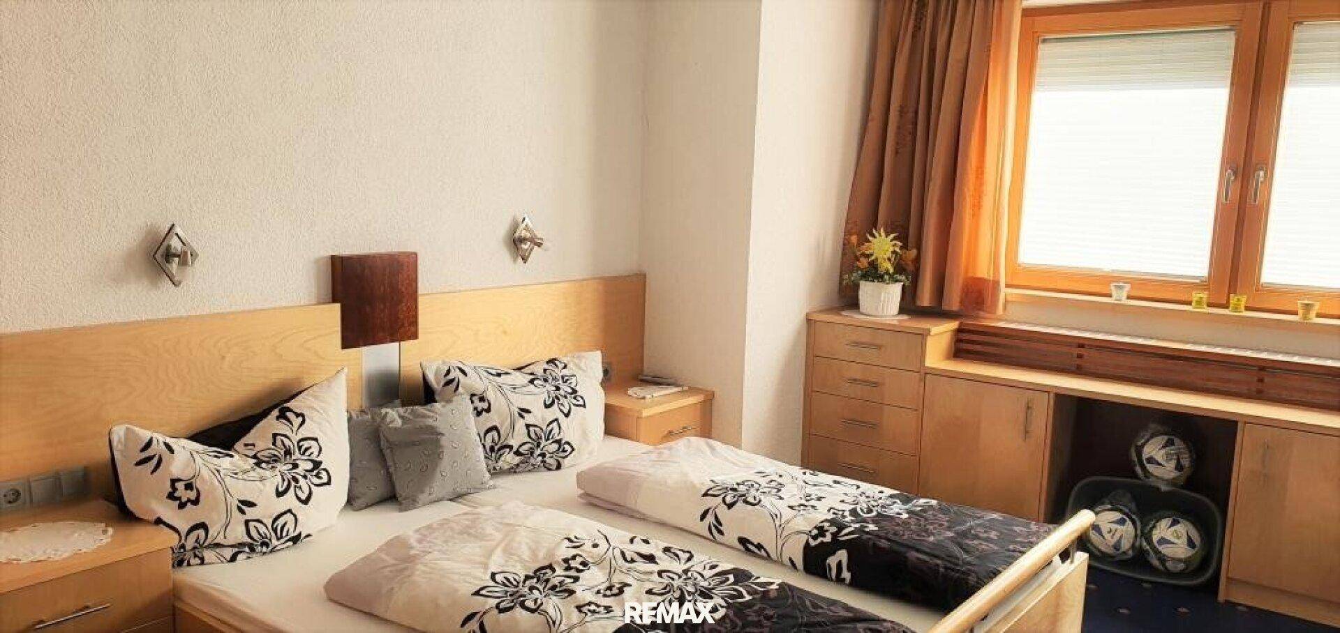 Schlafzimmer mit zwei Einzelbetten, Holzmöbeln und Fenster mit Jalousien.