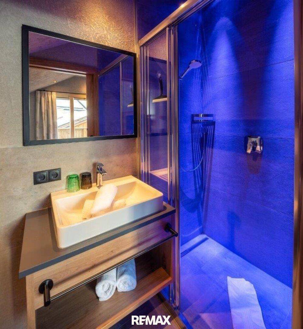 Modernes Badezimmer mit Einzelwaschbecken und einer Duschkabine mit stimmungsvoller blauer Beleuchtung.
