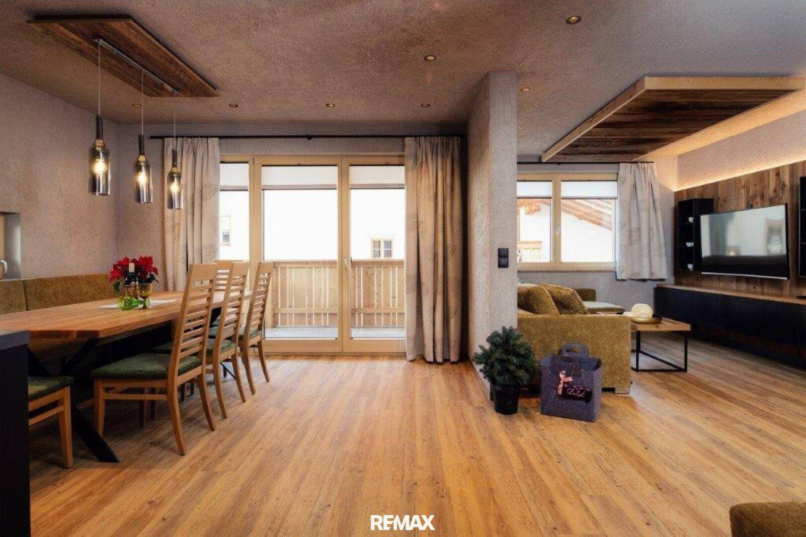 Geräumiger Wohn- und Essbereich mit Holzboden, Zugang zum Balkon und modernen Holzdetails an Decke und Wand.