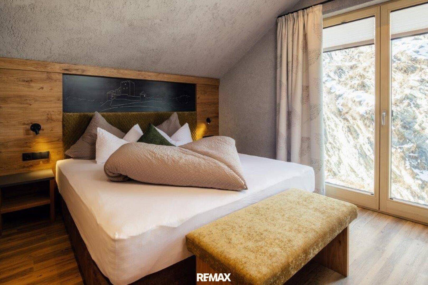 Schlafzimmer mit Holzboden, Dachschräge und großen Fenstern, die einen Blick auf die verschneite Berglandschaft bieten.