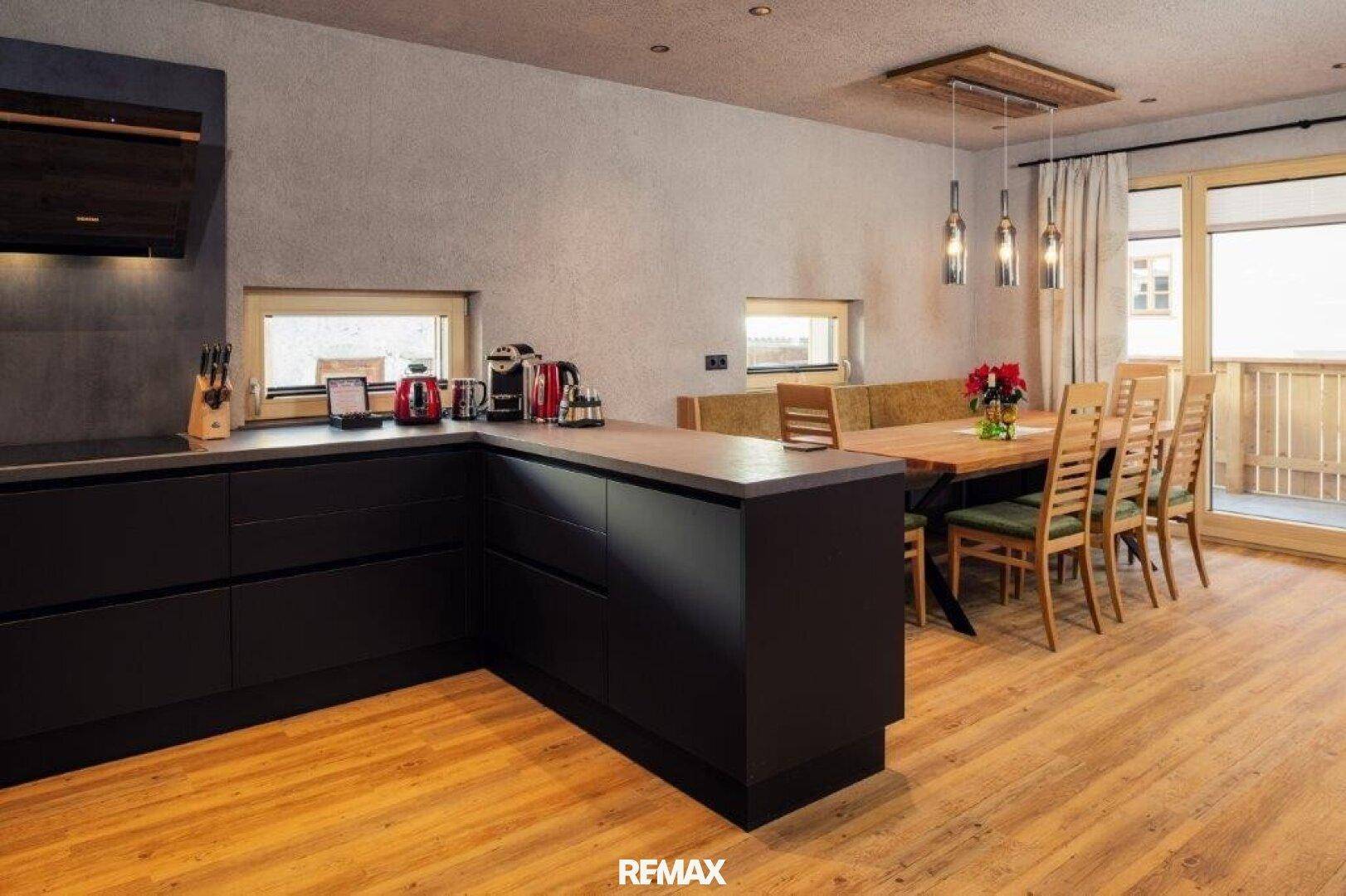 Moderne Küche mit schwarzen Unterschränken und einer Holztheke, offen zum Essbereich mit Holztisch.