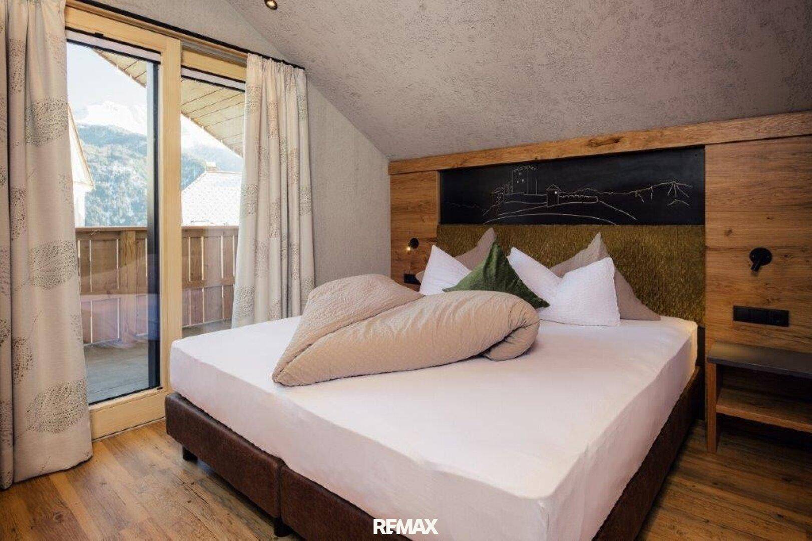 Schlafzimmer mit Holzboden, Dachschräge und Balkonzugang, der einen weiten Blick auf die Berge ermöglicht.