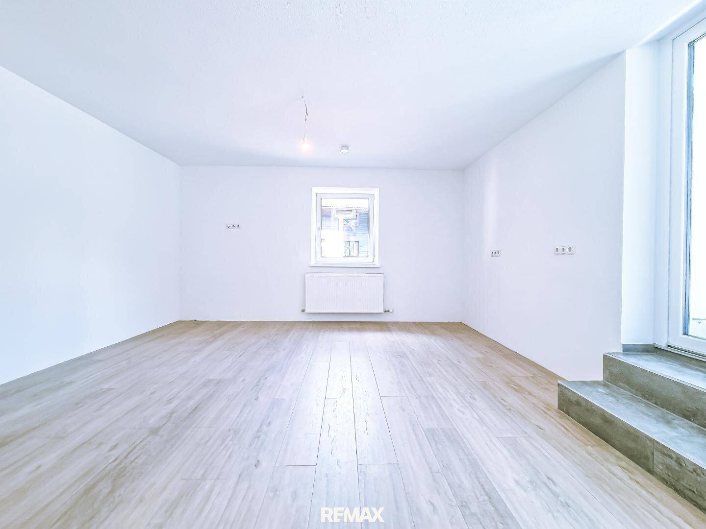 Heller, leerer Raum mit Holzoptik-Fliesenboden und einem Fenster, bereit zur individuellen Gestaltung.