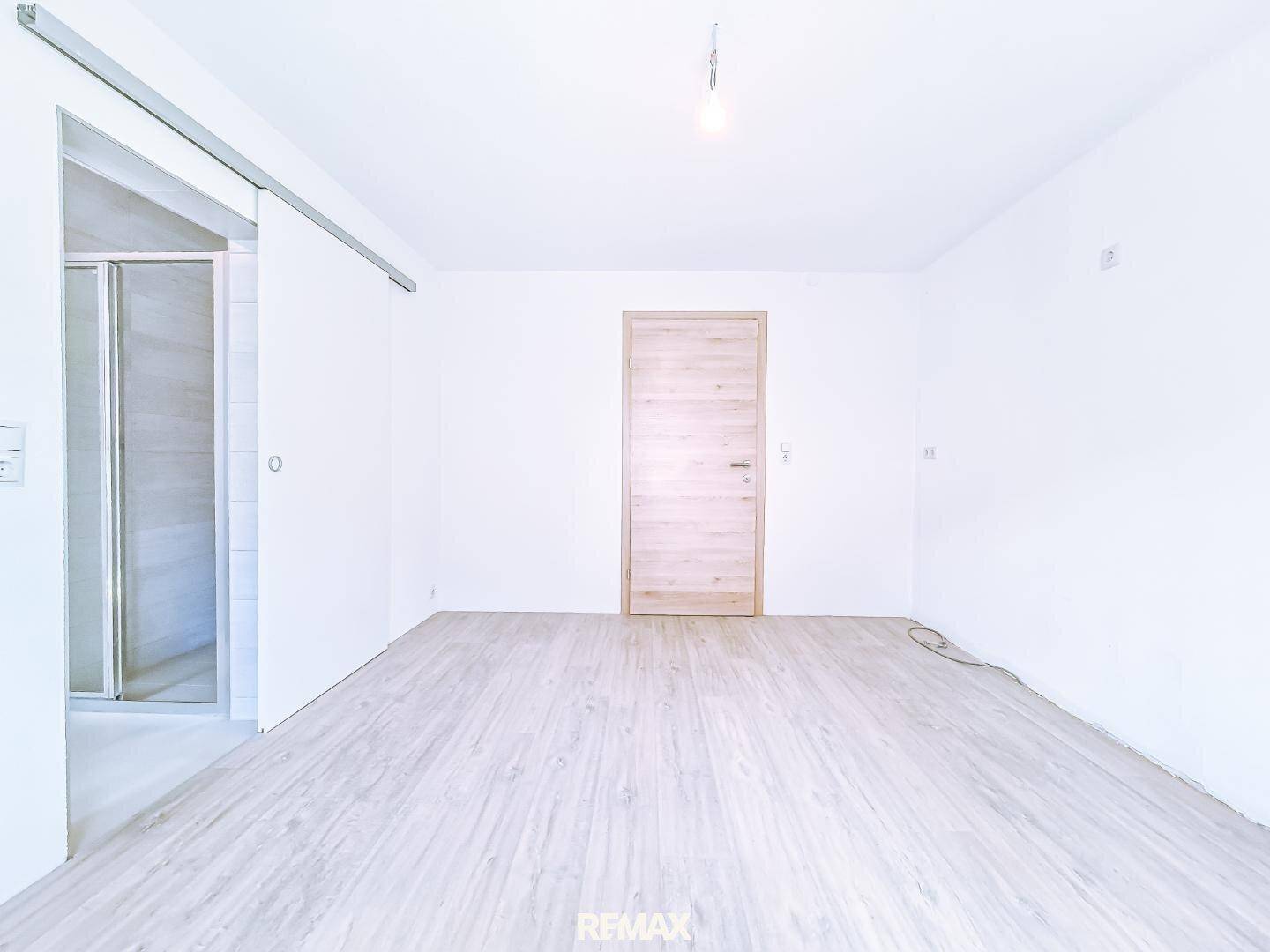 Leeres Schlafzimmer mit hellem Fliesenboden in Holzoptik und moderner Schiebetür.