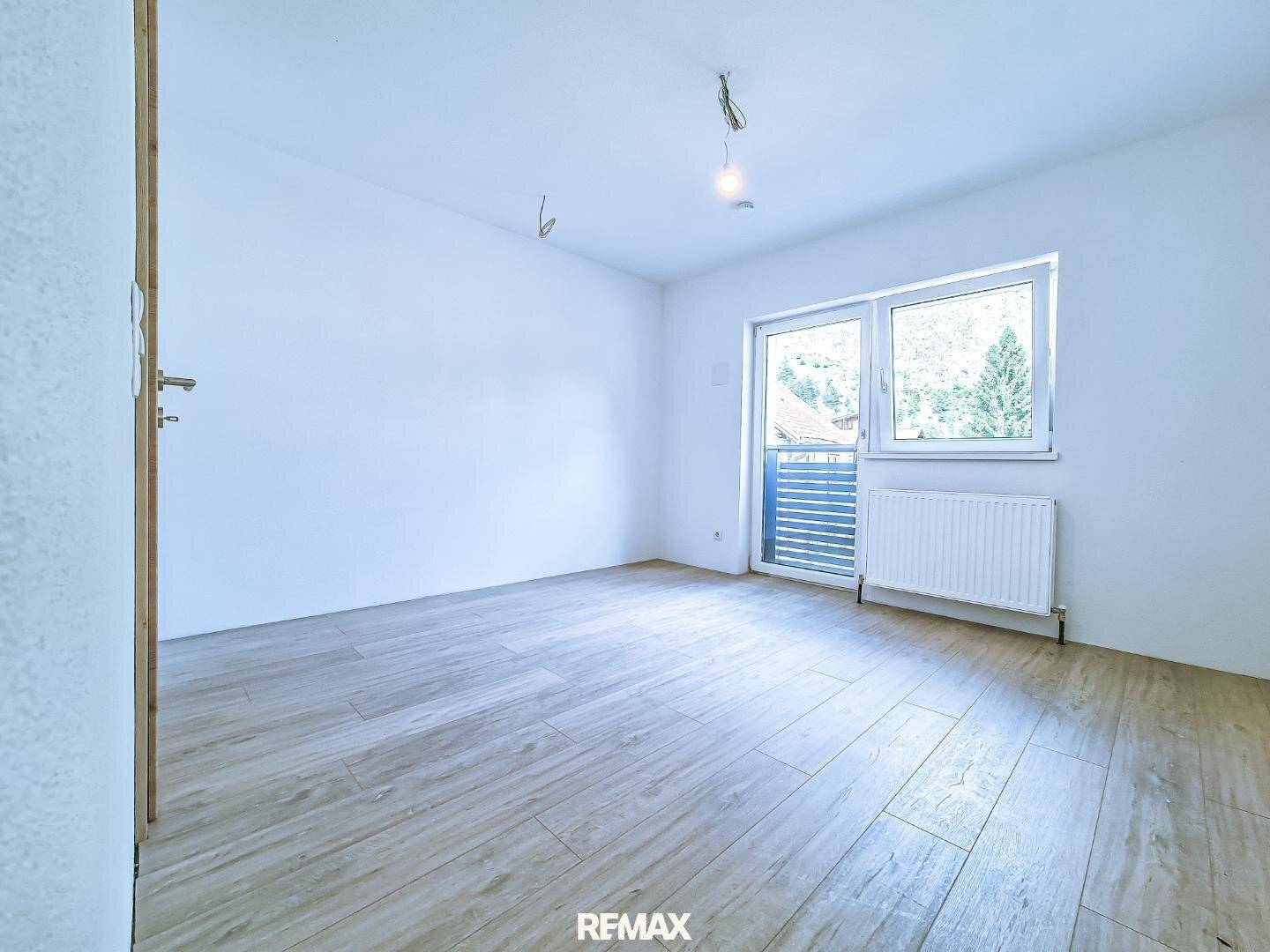 Helles Schlafzimmer mit Fliesenboden in Holzoptik und Zugang zu einem französischen Balkon.