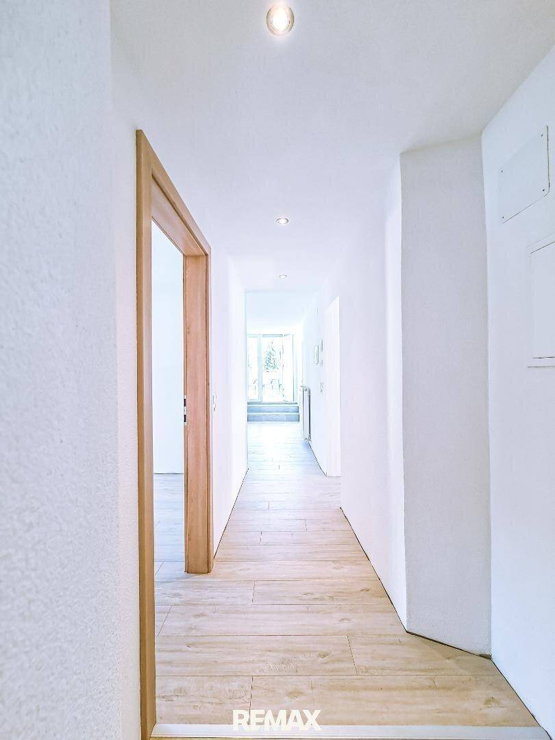 Langer, heller Flur mit Fliesenboden in Holzoptik und Holztüren, der zu weiteren Räumen führt.
