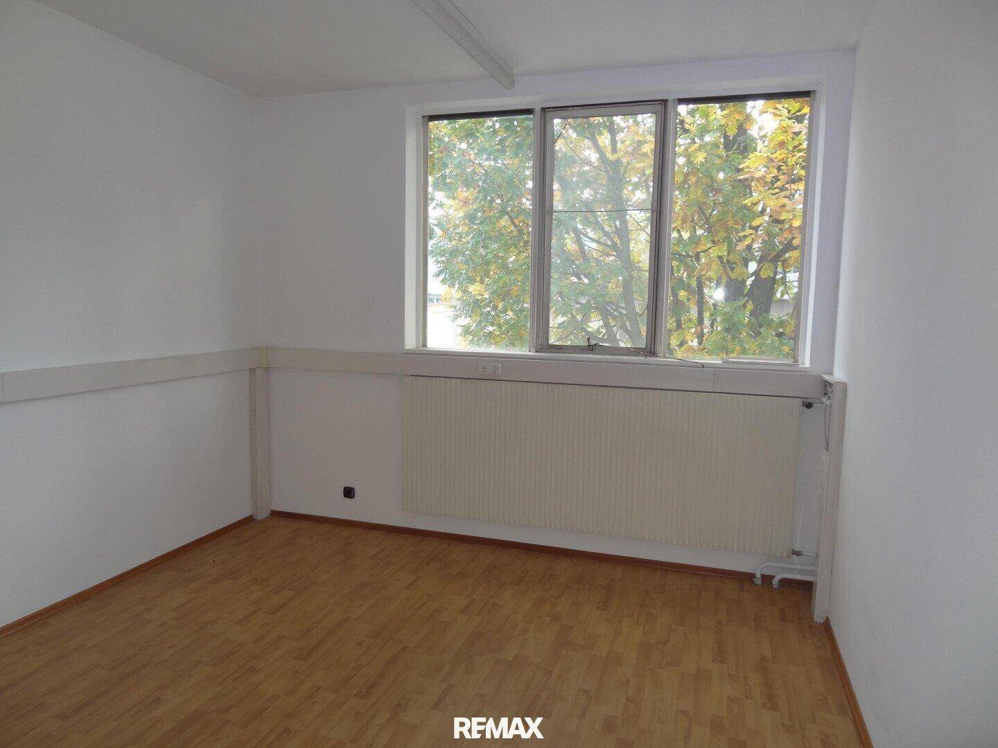 Kleinerer Büroraum mit Laminatboden, großen Fenstern und einem schönen Blick auf Bäume.
