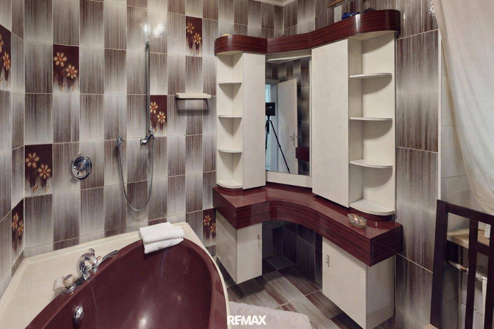 Badezimmer mit braunen Fliesen, Badewanne und integriertem Waschtisch im 80er-Jahre-Stil.