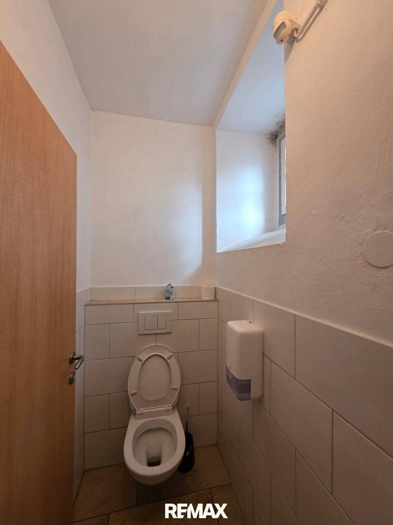 Einfache Toilette mit weiß gefliesten Wänden und kleinem Fenster für gute Belüftung.