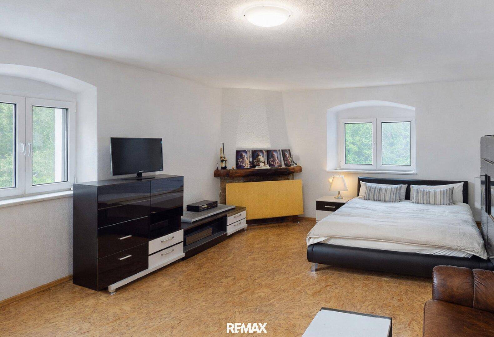 Geräumiges Wohnzimmer mit Bett, TV-Möbeln und zwei Fenstern, vielseitig nutzbar.