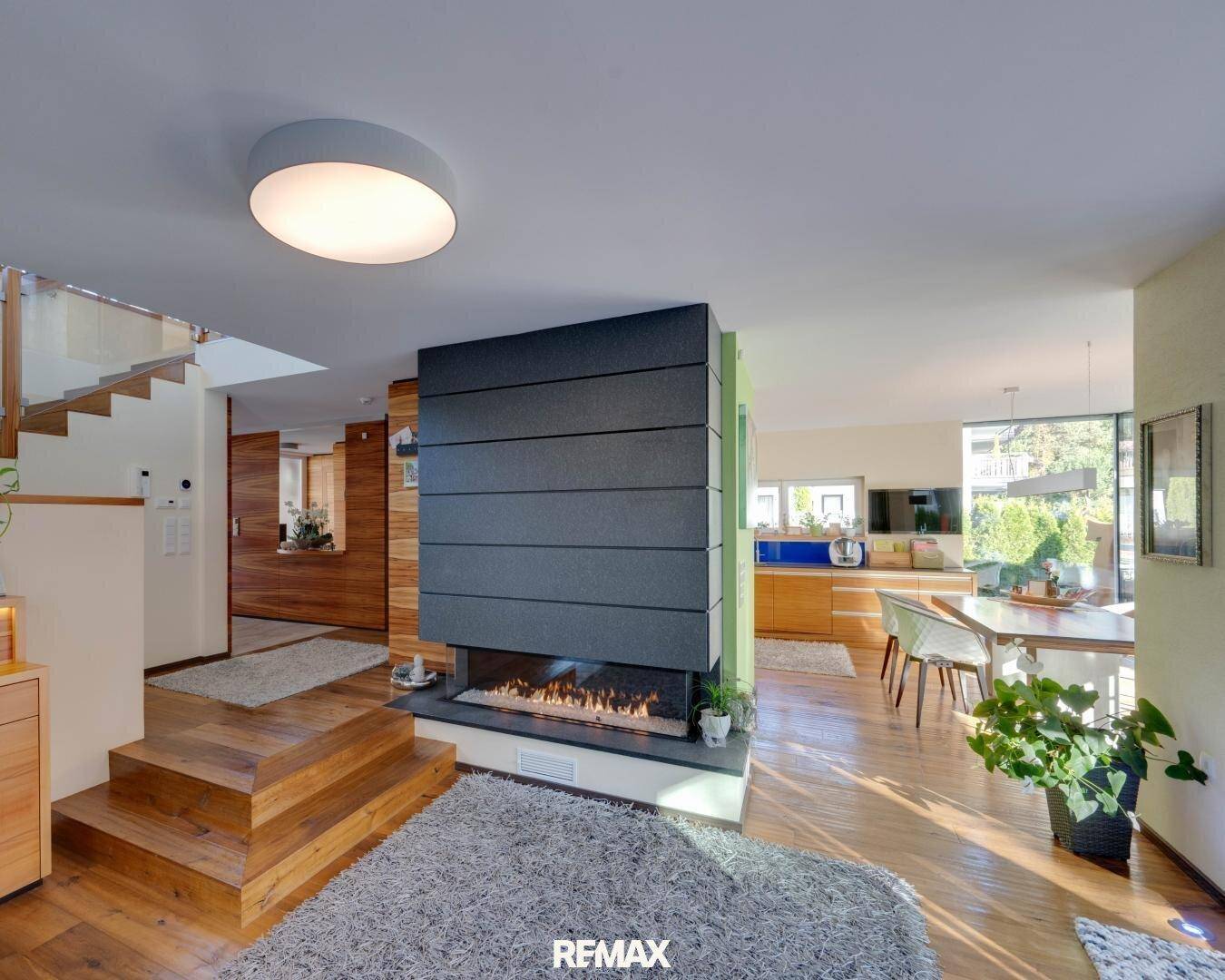 Heller Wohn- und Essbereich mit modernem Kamin, Holztreppe und Parkettboden.