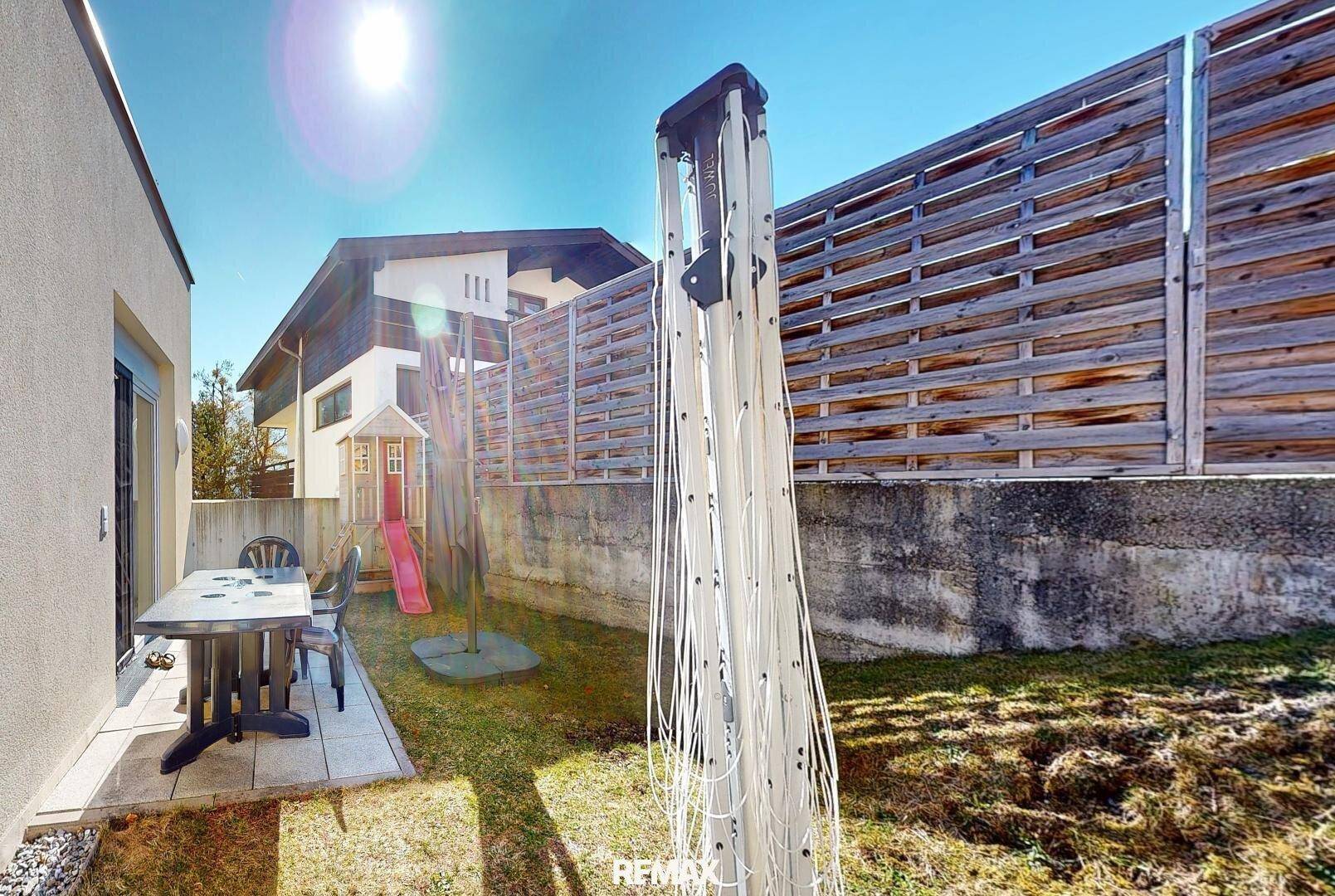 Sonniger Garten mit Rasenfläche, Wäscheständer und einem kleinen Spielhaus für Kinder.